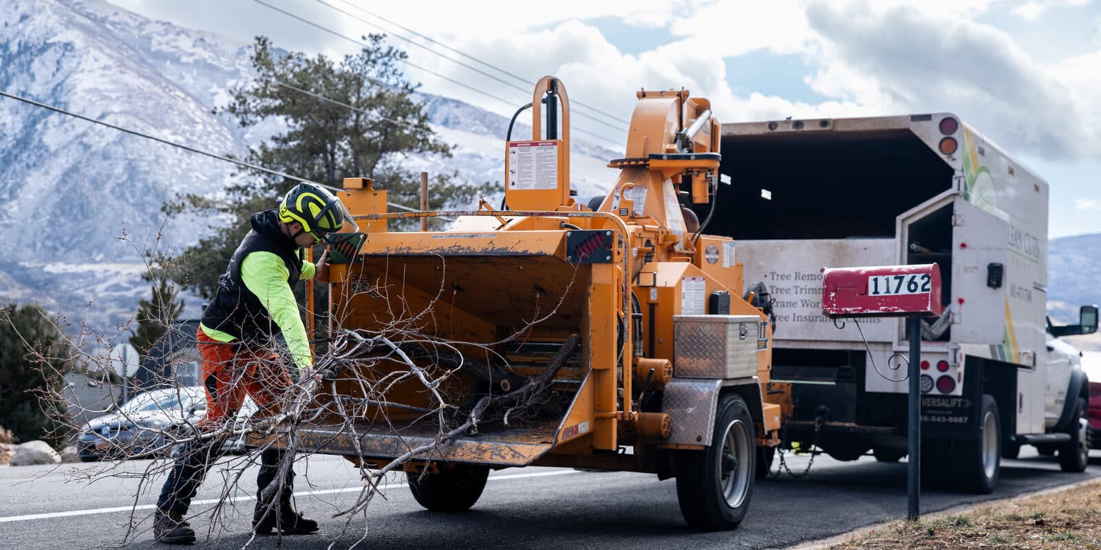 Clean Cuts Trees crew feeding brush into the chipper beside their truck on a Utah street